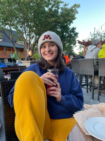 A University of Minnesota student smiling and wearing a UMN beanie, navy sweater and gold sweatpants.