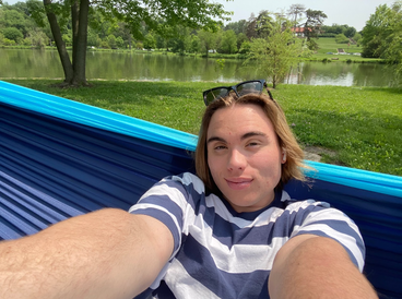 A smiling University of Minnesota student wearing a blue and white horizontal stripped shirt, sunglasses on head, and sitting in a hammock.