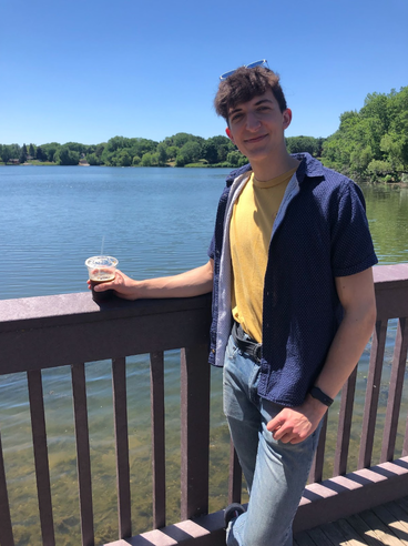 A smiling University of Minnesota student leaning against a fence over a lake.