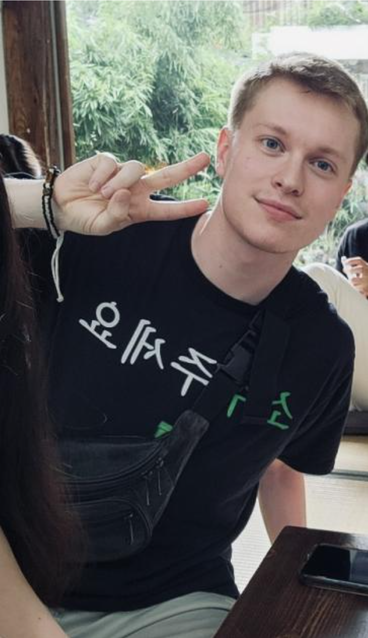 A student holding a peace sign, smiling and wearing a black t-shirt.